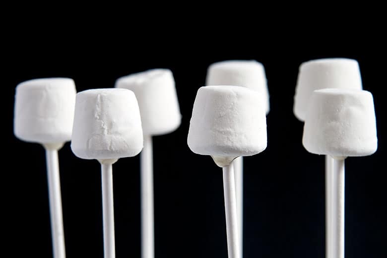White marshmallows stuck on cake pop sticks on a black background
