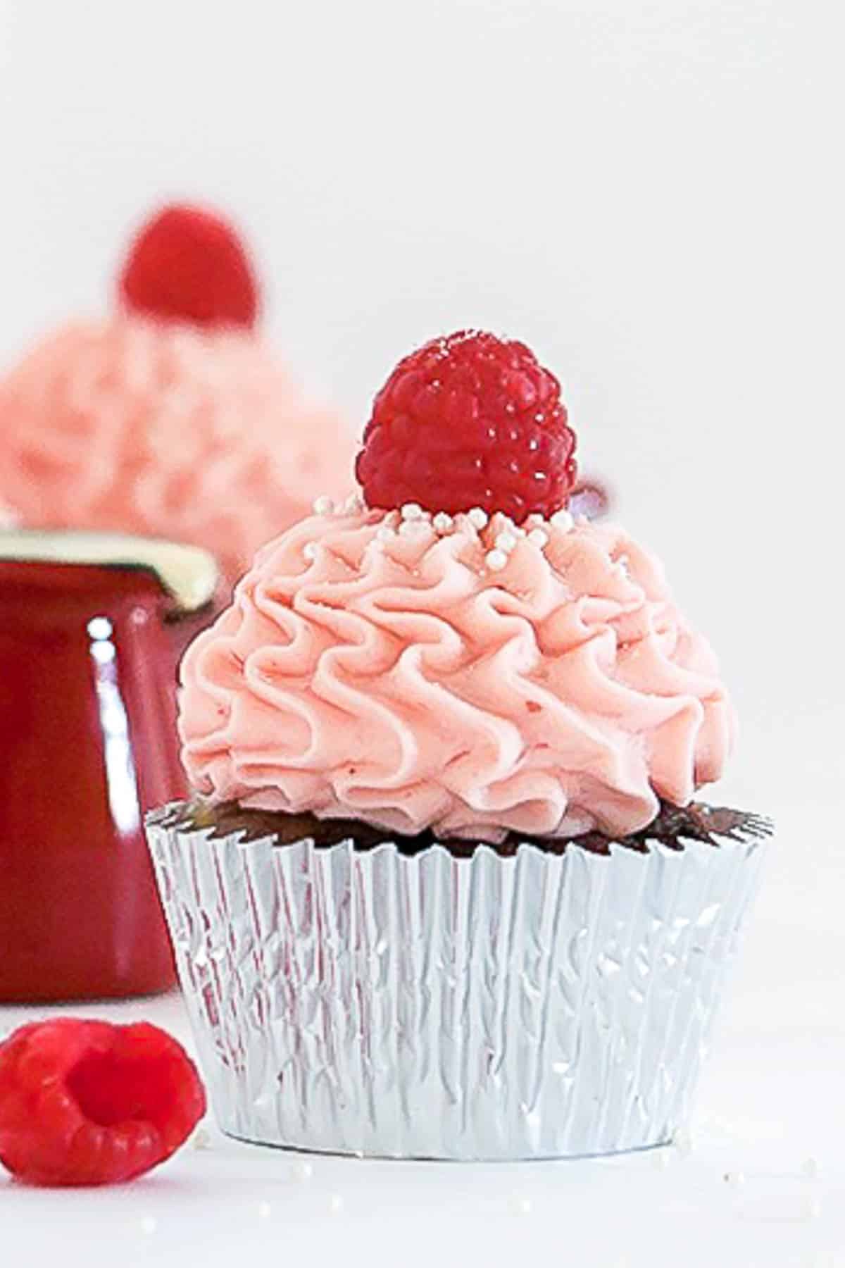 Chocolate raspberry cupcake iced with pink buttercream and topped with a fresh raspberry