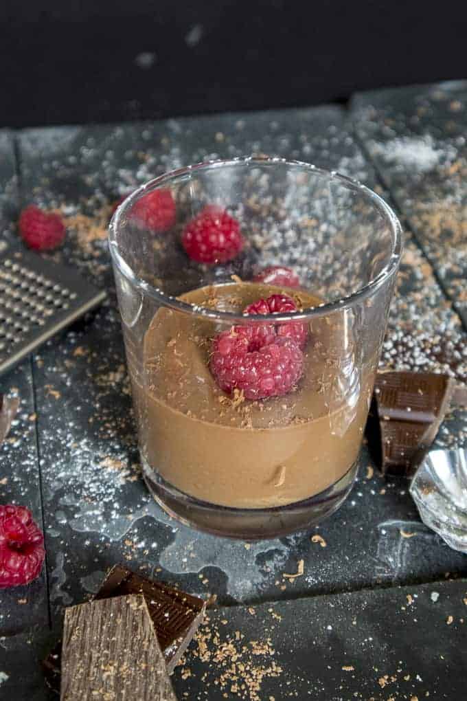 Chocolate pudding in a glass with fresh raspberries on top and a sprinkle of icing sugar