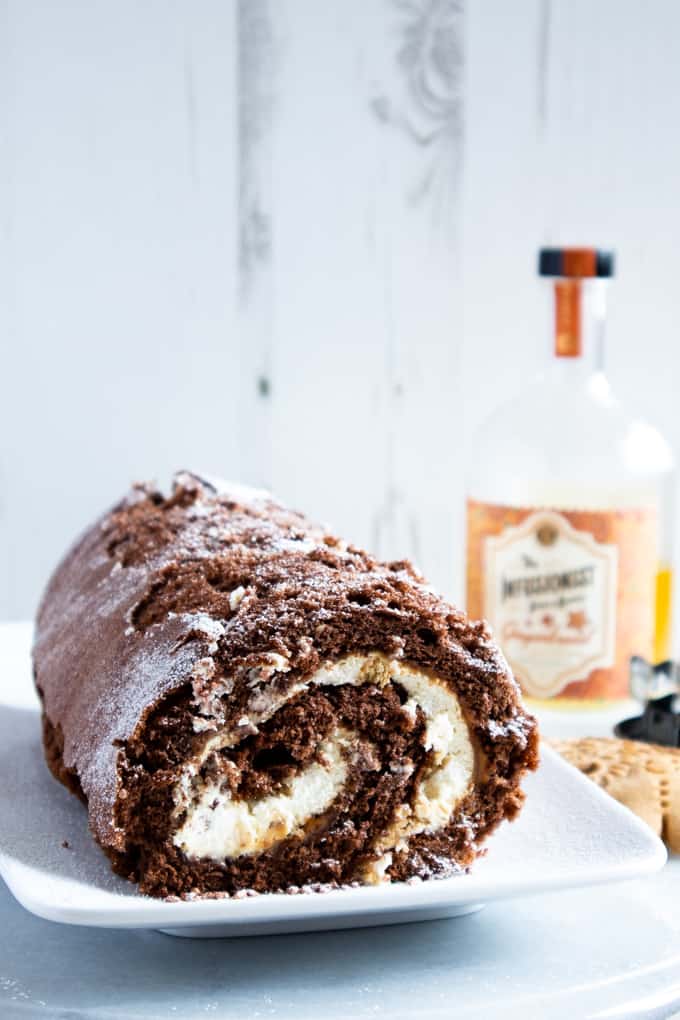 A chocolate and gingerbread roulade cake, on a plate dusted with icing sugar