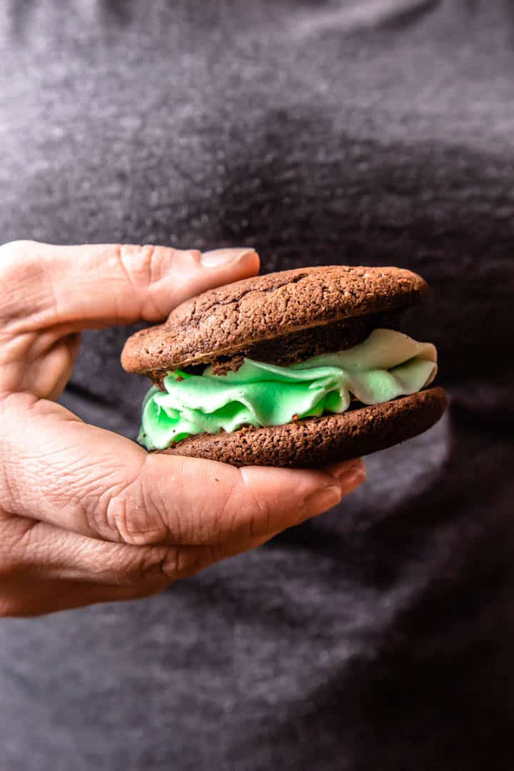 A hand holding a chocolate whoopie pie filled with green mint buttercream frosting