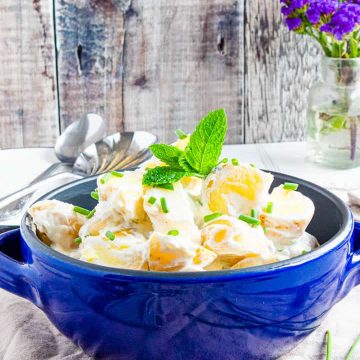 Blue bowl filled with easy low fat potato salad topped with chopped chives and a spring of mint