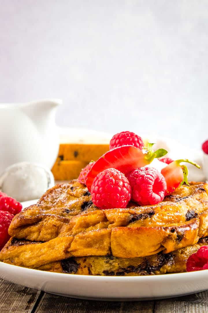 Close up of a stack of golden french toast with mixed summer fruits and creme fraiche on top