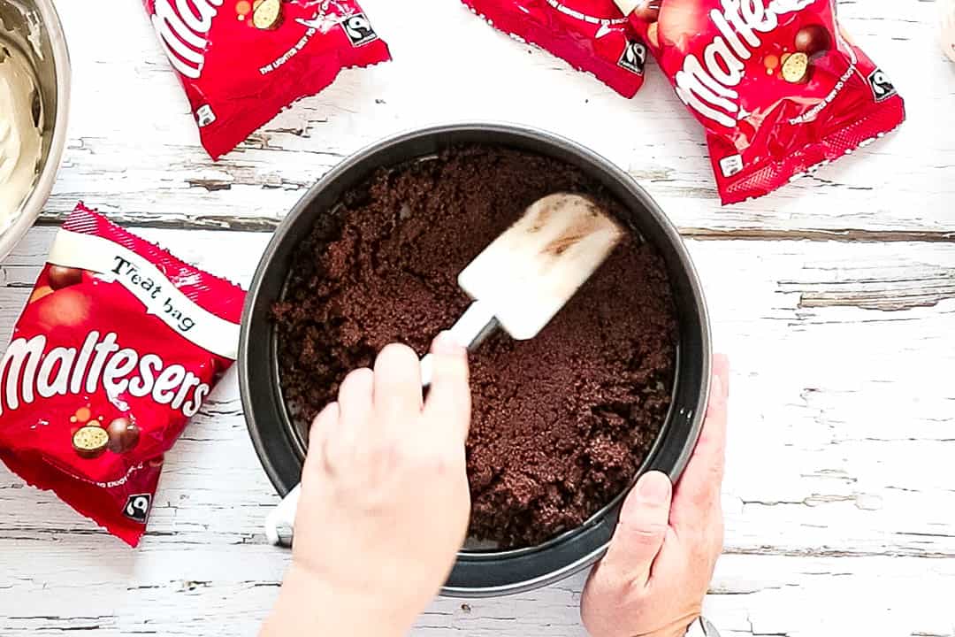 Smoothing the biscuit crumbs into a cake tin