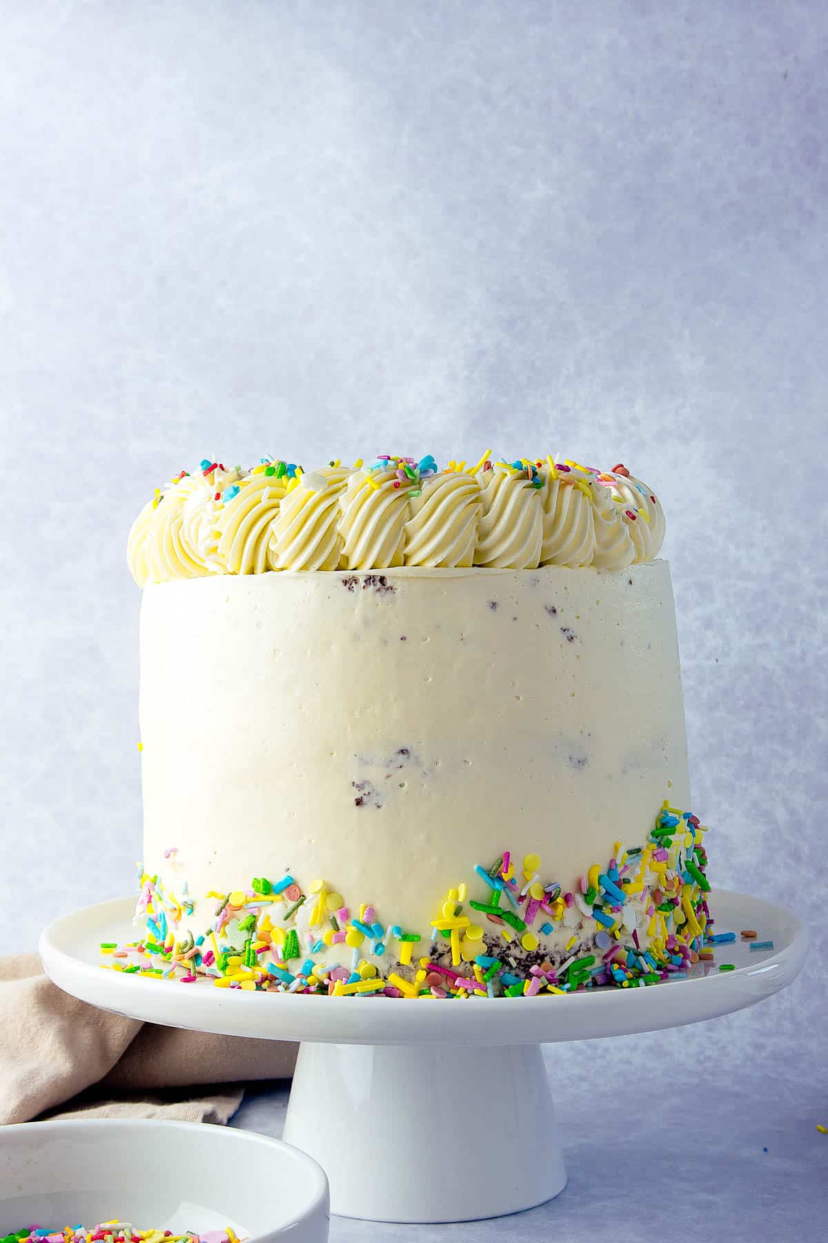 Vanilla cake iced with buttercream and stood on a white cake stand