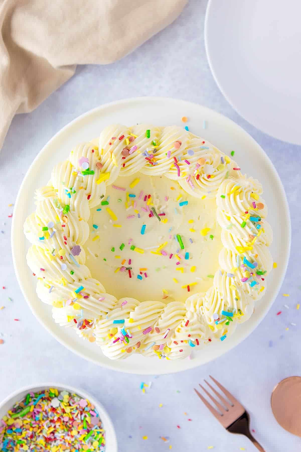 Looking down on top of a white cake, rainbow sprinkles are scattered on top
