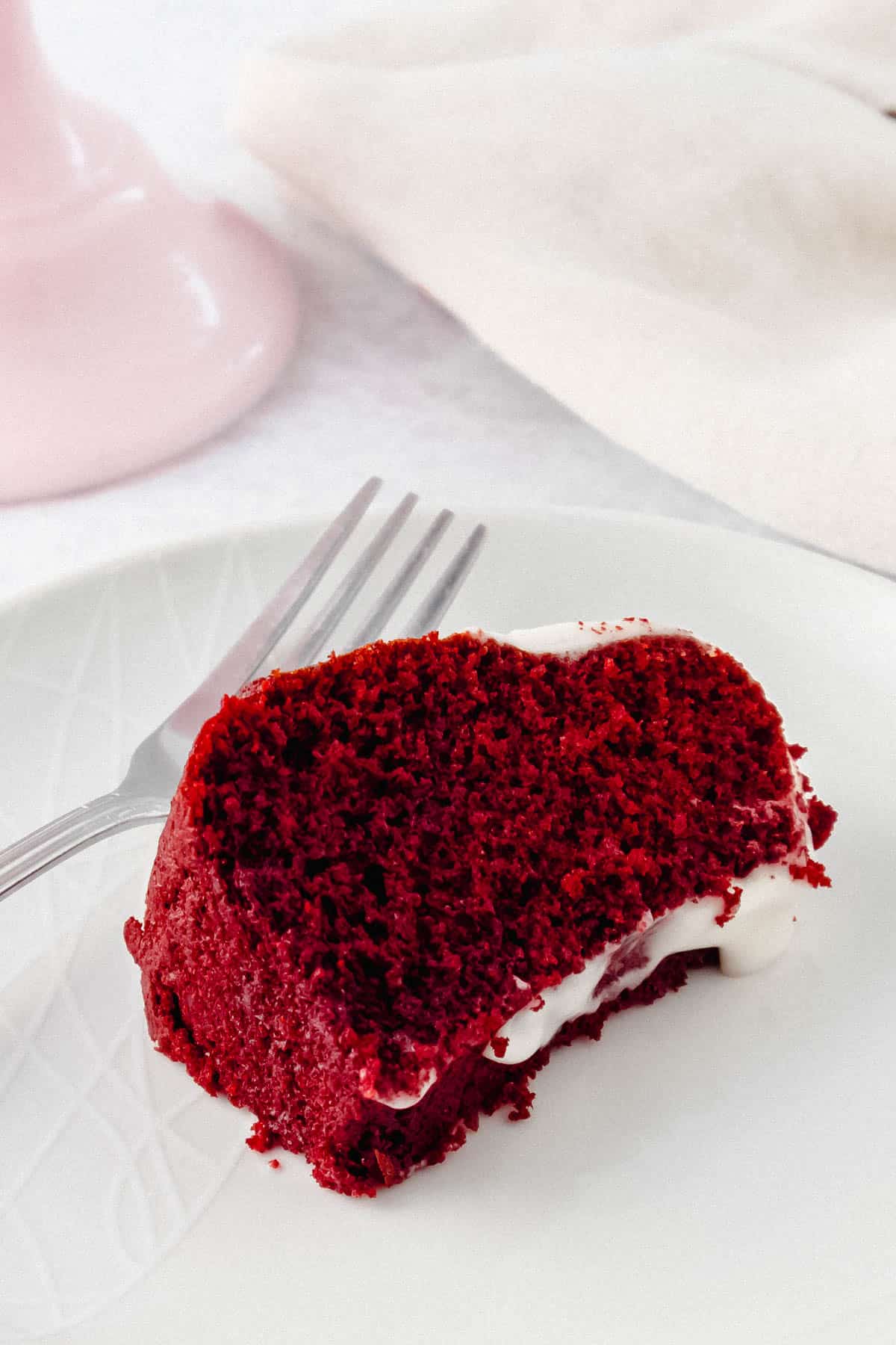 Slice of red coloured cake on a plate with a fork