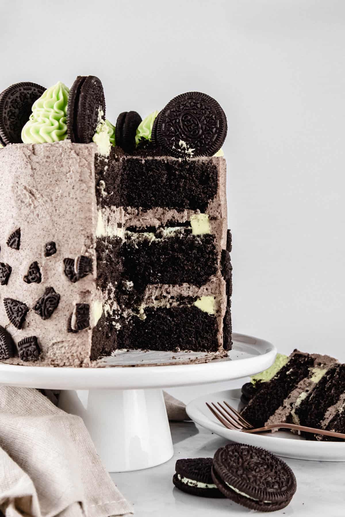 Mint Oreo cake on a white cake stand with a slice cut out