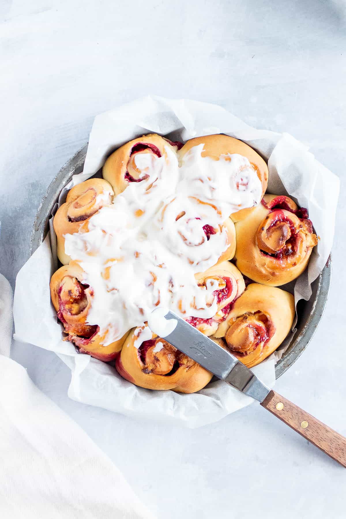 Overhead view of a round pan filled with lemon raspberry swirl rolls partly iced with white icing glaze