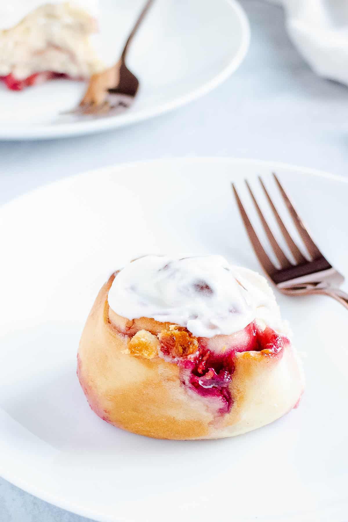 Glazed raspberrry swirl roll on a white plate with fork