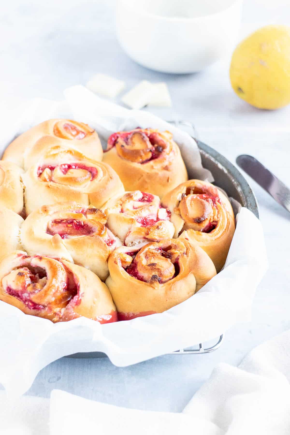 Round cake pan lined with baking paper, and filled with baked raspberry swirl rolls