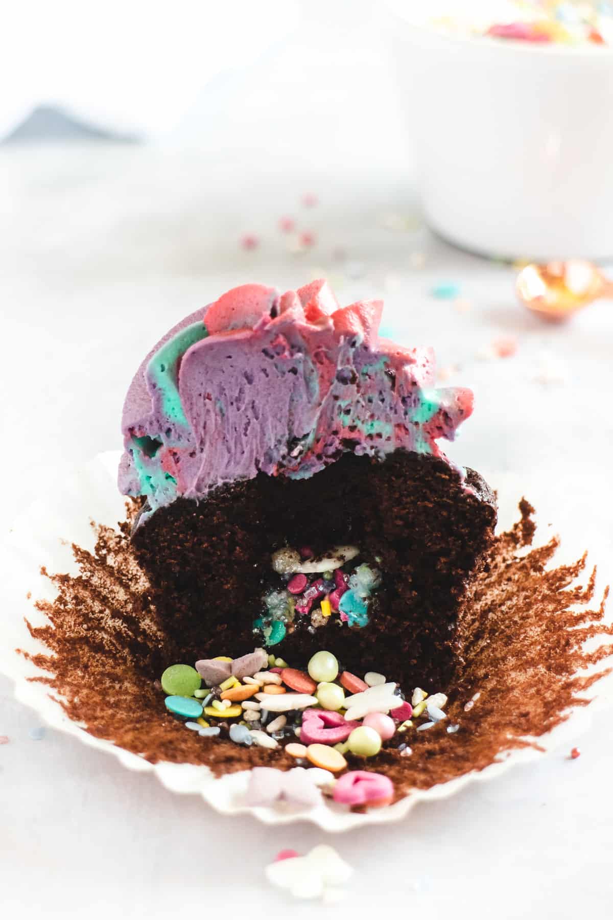 Rainbow pinata cupcake cut in half with sprinkles pouring out of the middle
