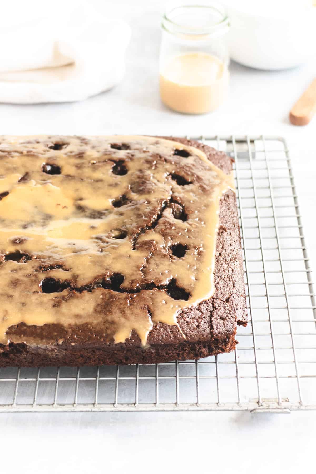 Chocolate cake on a wire cooling rack with holes poked in the top and caramel poured over