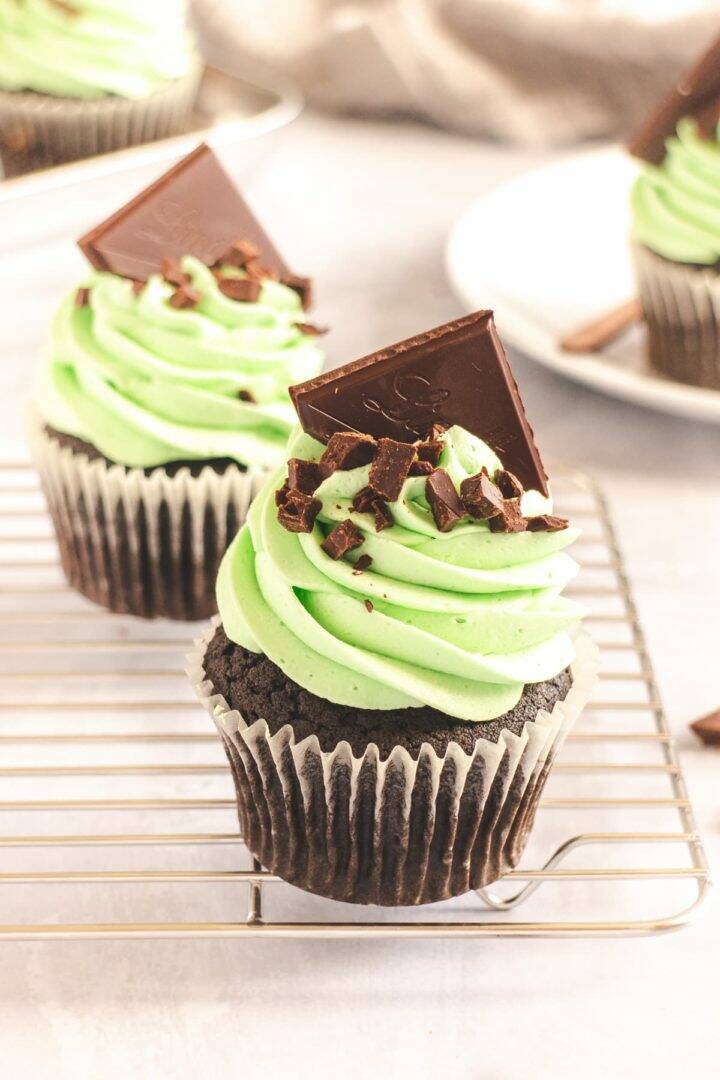 Two chocolate cupcake on a wire cooling rack, decorated with mint frosting and dark chocolate