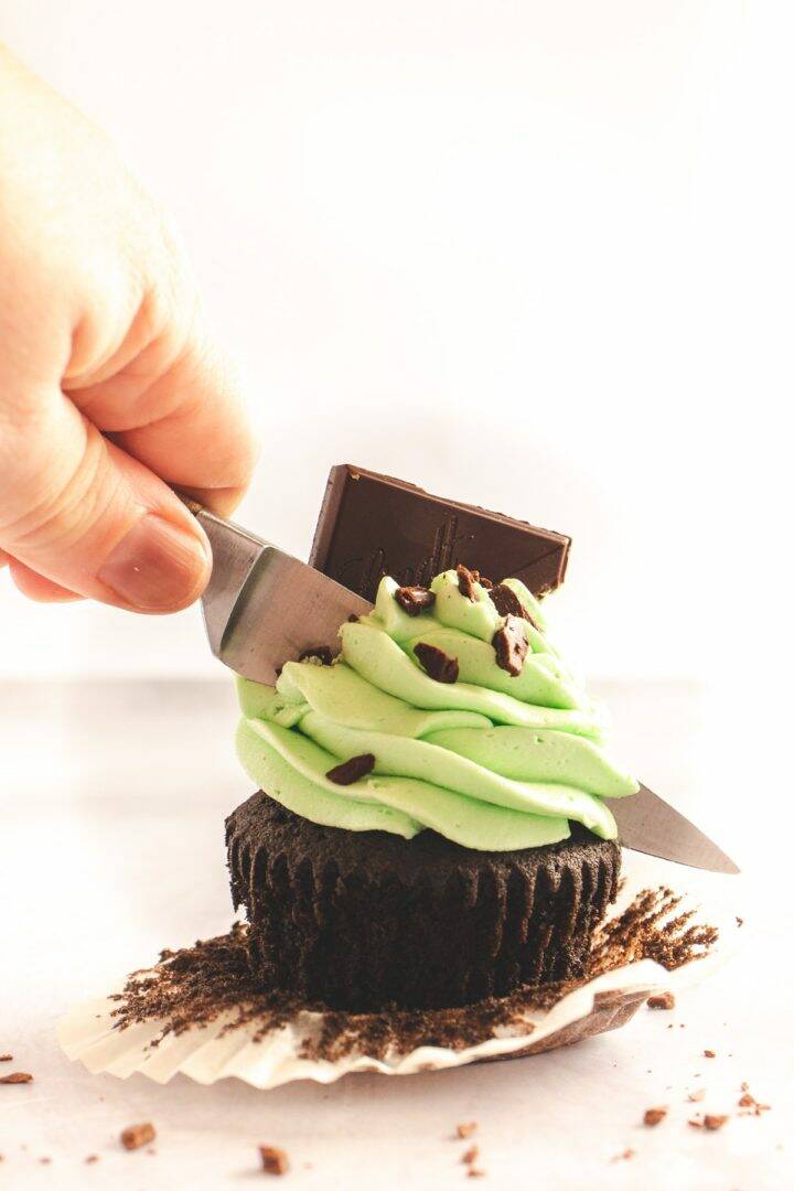 Chocolate cupcake with mint green frosting being sliced in half with a knife