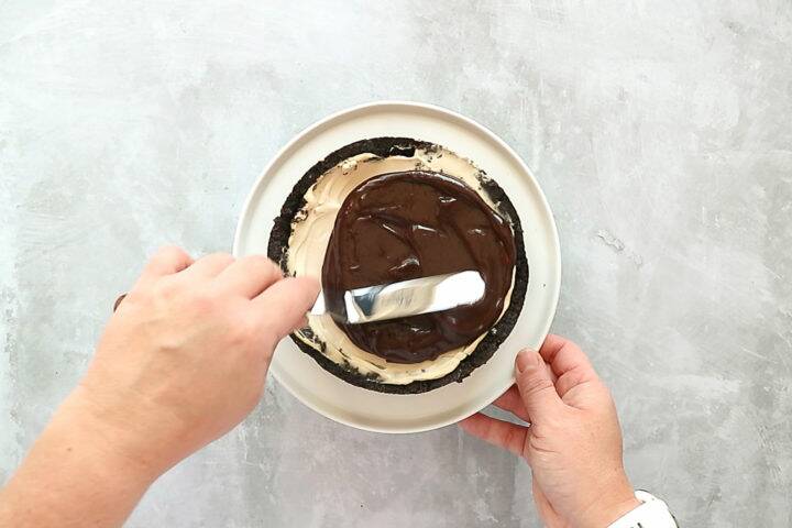 Smoothing melted chocolate over a cheesecake with a spatula