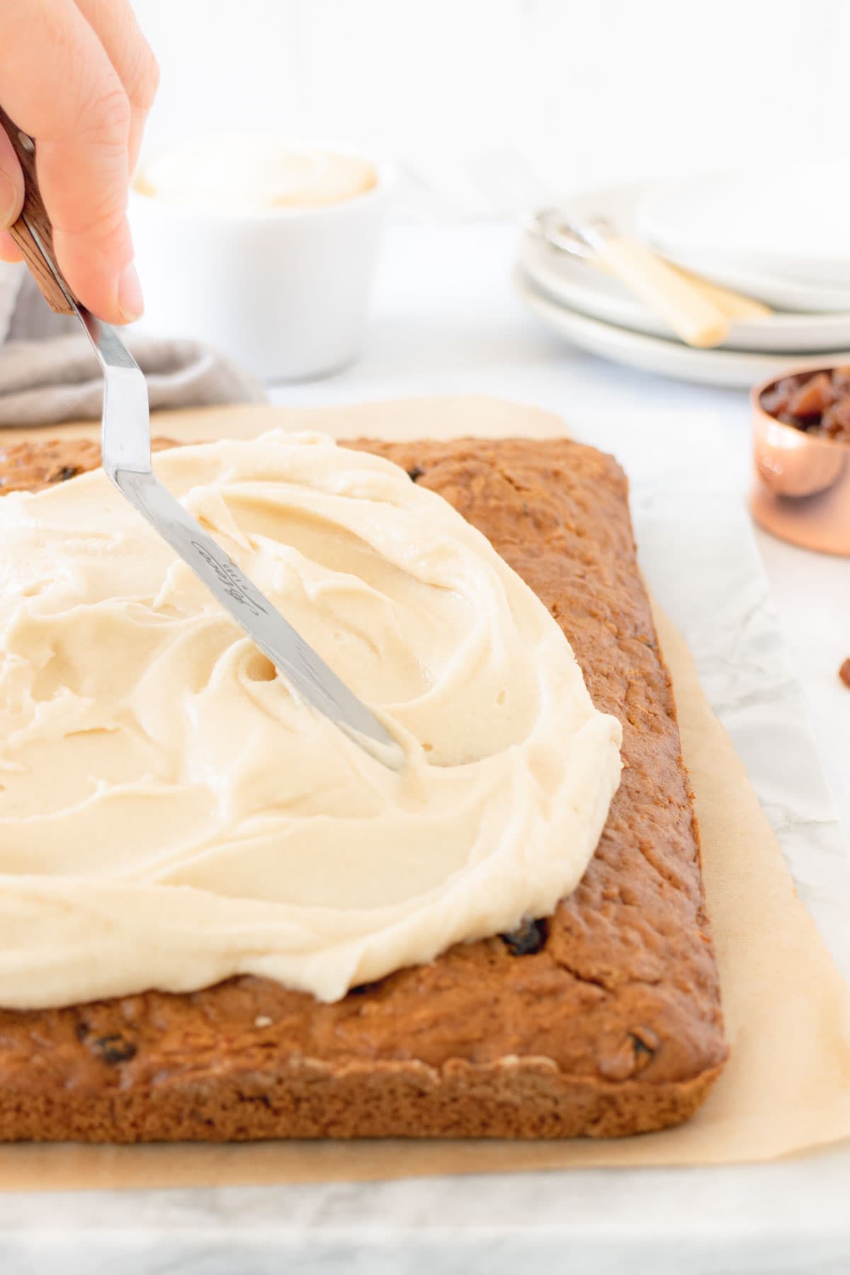 Smoothing cream cheese frosting on top of a carrot tray bake cake