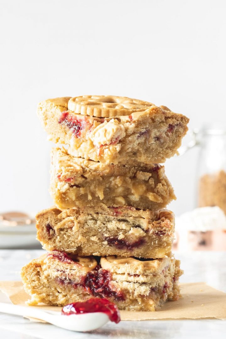 Stack of gooey jammie dodger blondies on with a spoon of raspberry jam