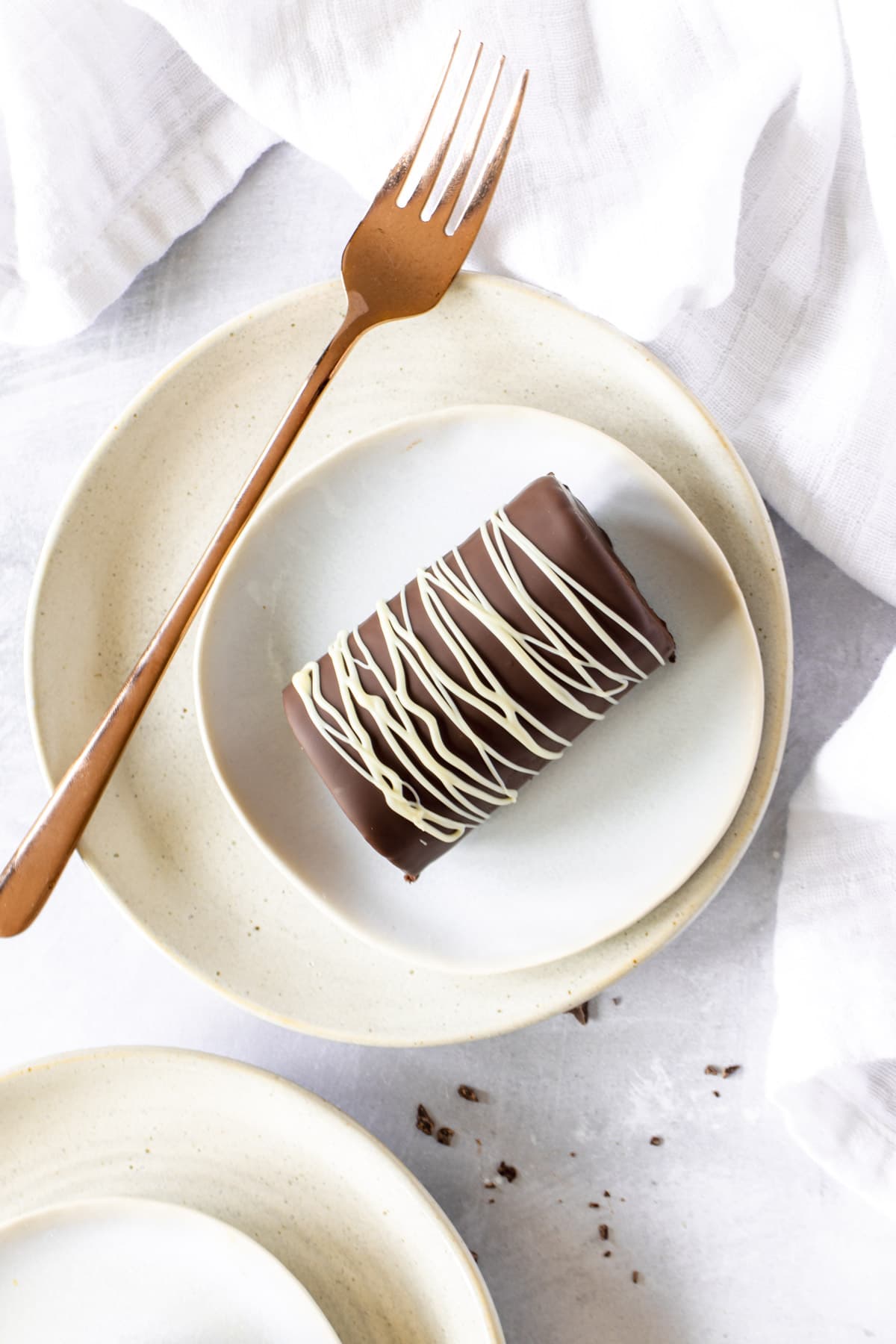 Overhead view of a chocolate mini roll drizzled with white chocolate on two stacked plates with a fork