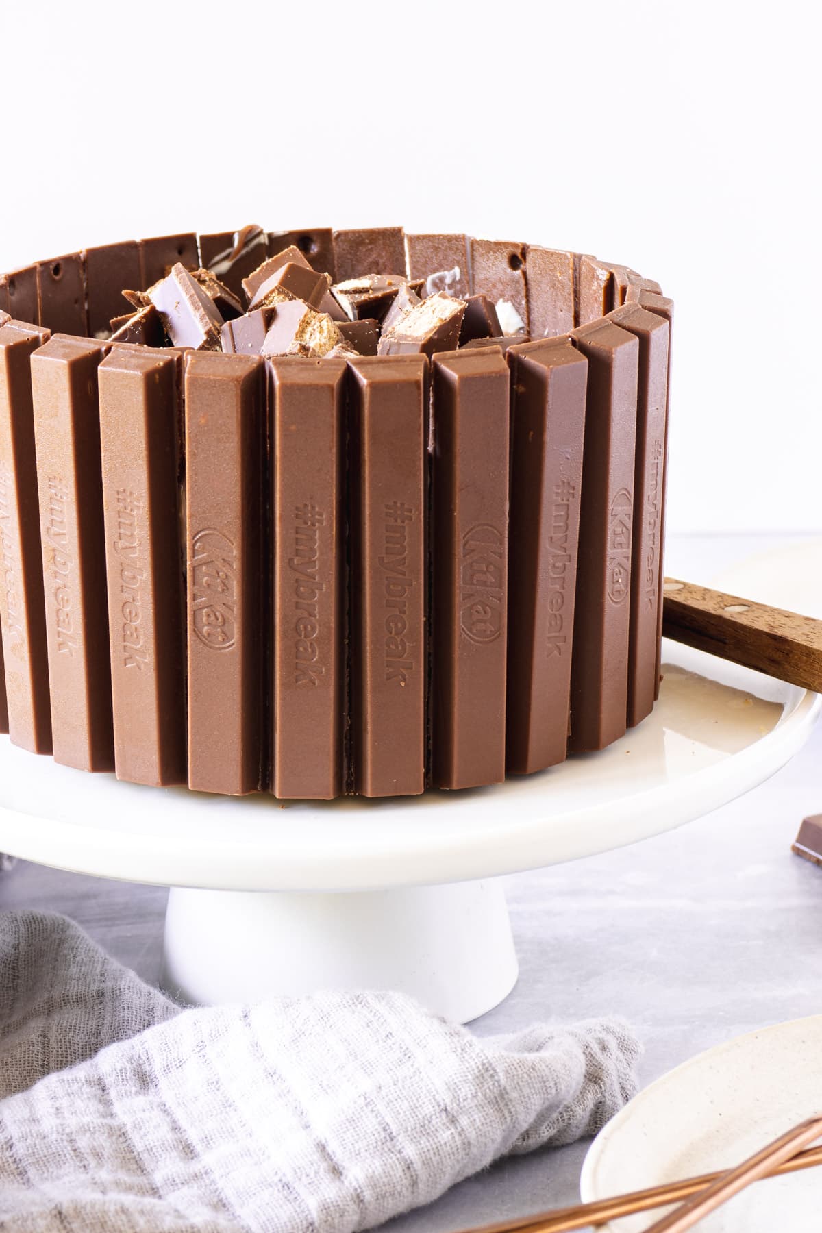 Chocolate cheesecake surrounded with chocolate wafer fingers on a white cake stand