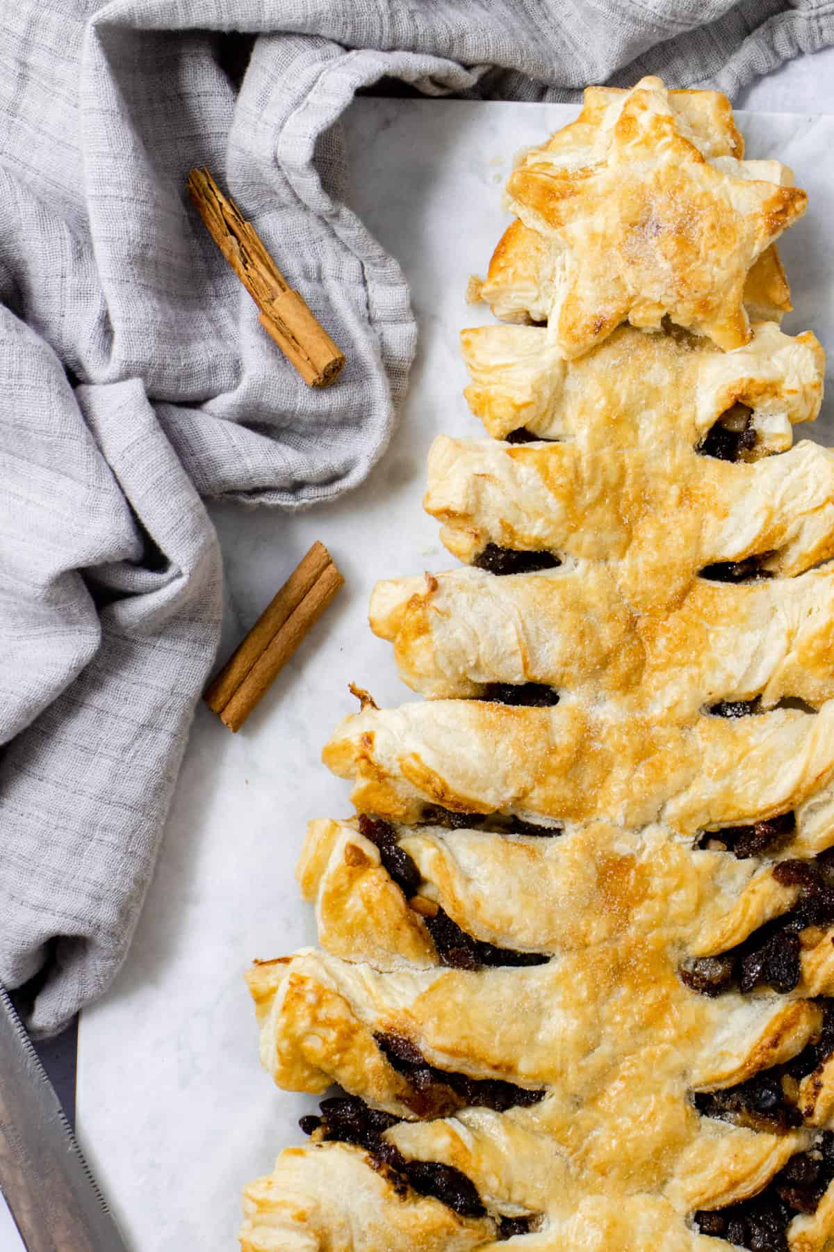 Close up of mincemeat puff pastry Christmas tree surrounded by cinnamon sticks