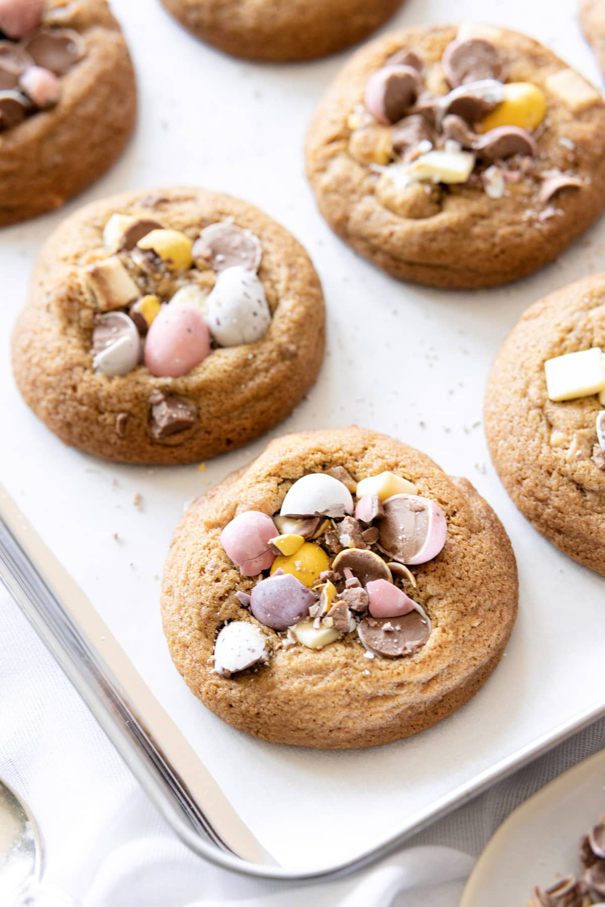 Close up of a cookie topped with white chocolate chunks and mini eggs on a baking sheet