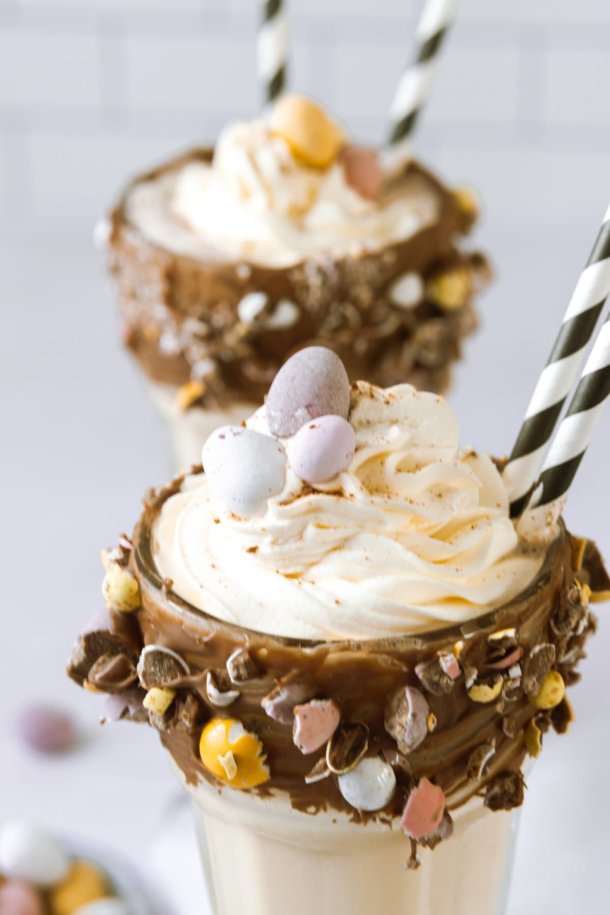 Whipped cream on top of a milkshake glass, coated in chocolate and dipped in crushed chocolate eggs