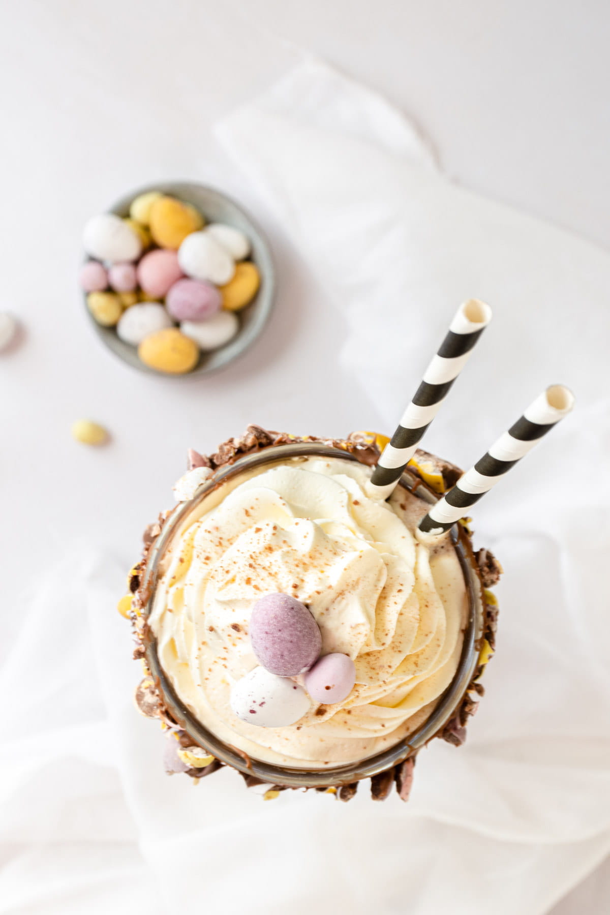 Top down shot of vanilla milkshake with black and white striped straws and Easter chocolate eggs