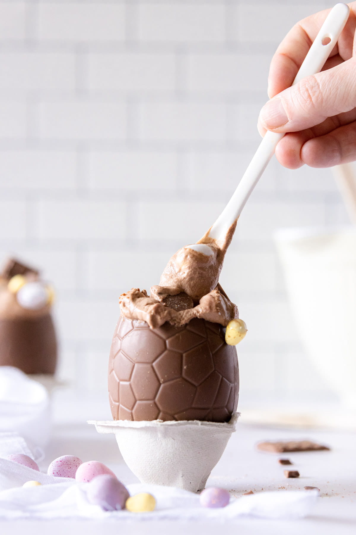 Hand holding a white spoon dipped in chocolate egg mousse