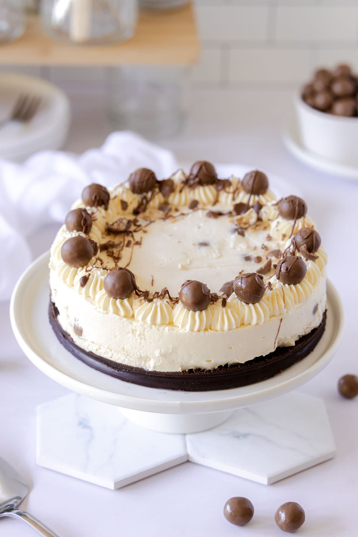 Cheesecake on a white plate topped with Maltesers and drizzled with chocolate