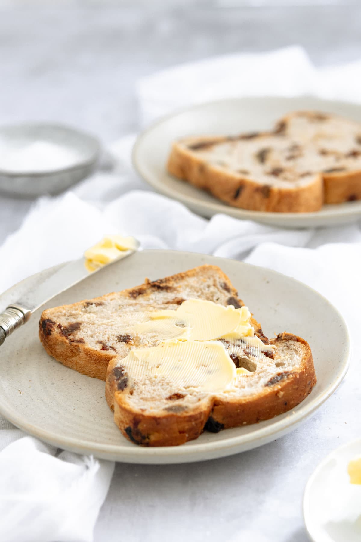 A slice of fruit loaf on a plate spread with unsalted butter