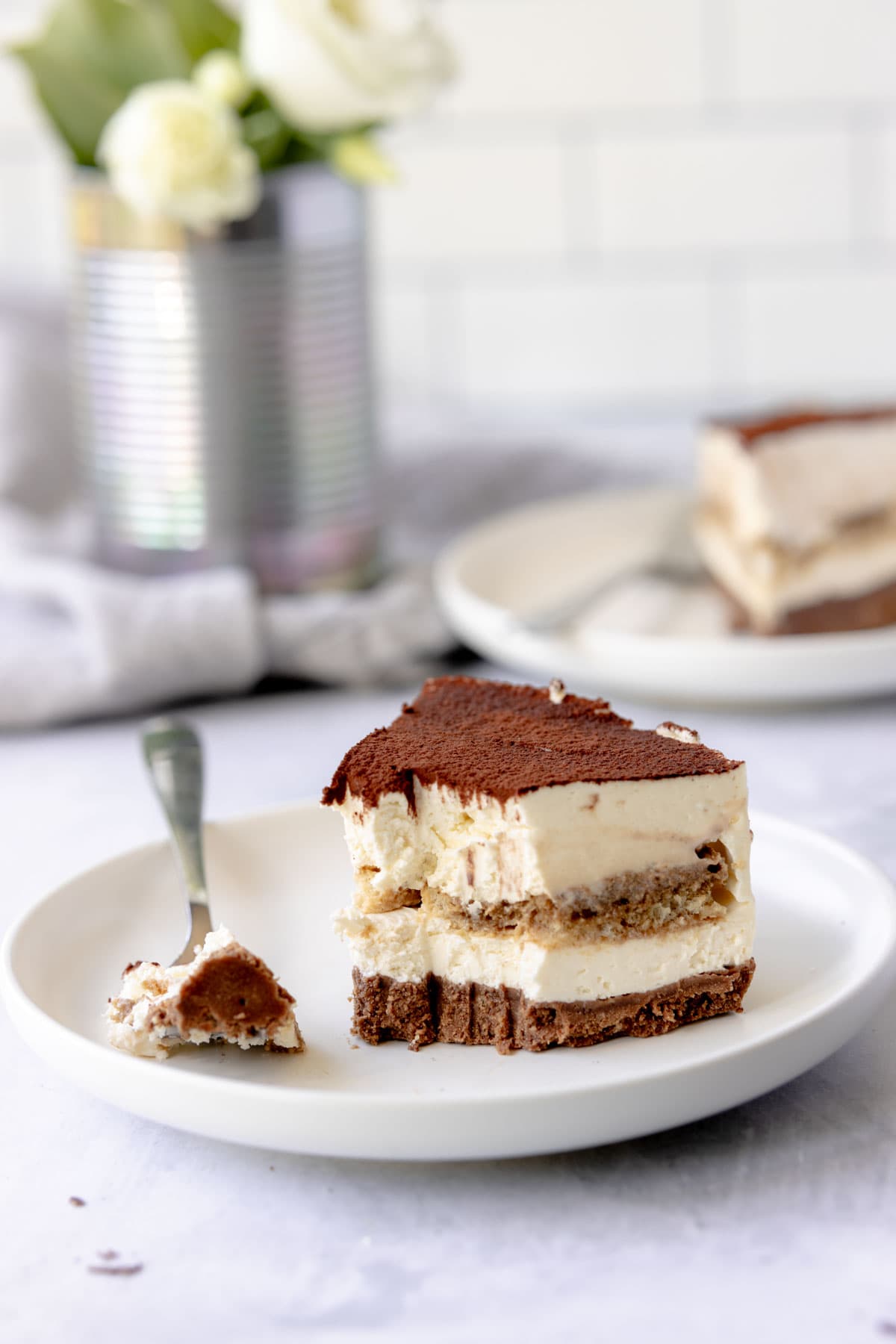 Slice of Tiramisu cheesecake on a plate with a fork and a piece of cheesecake on it