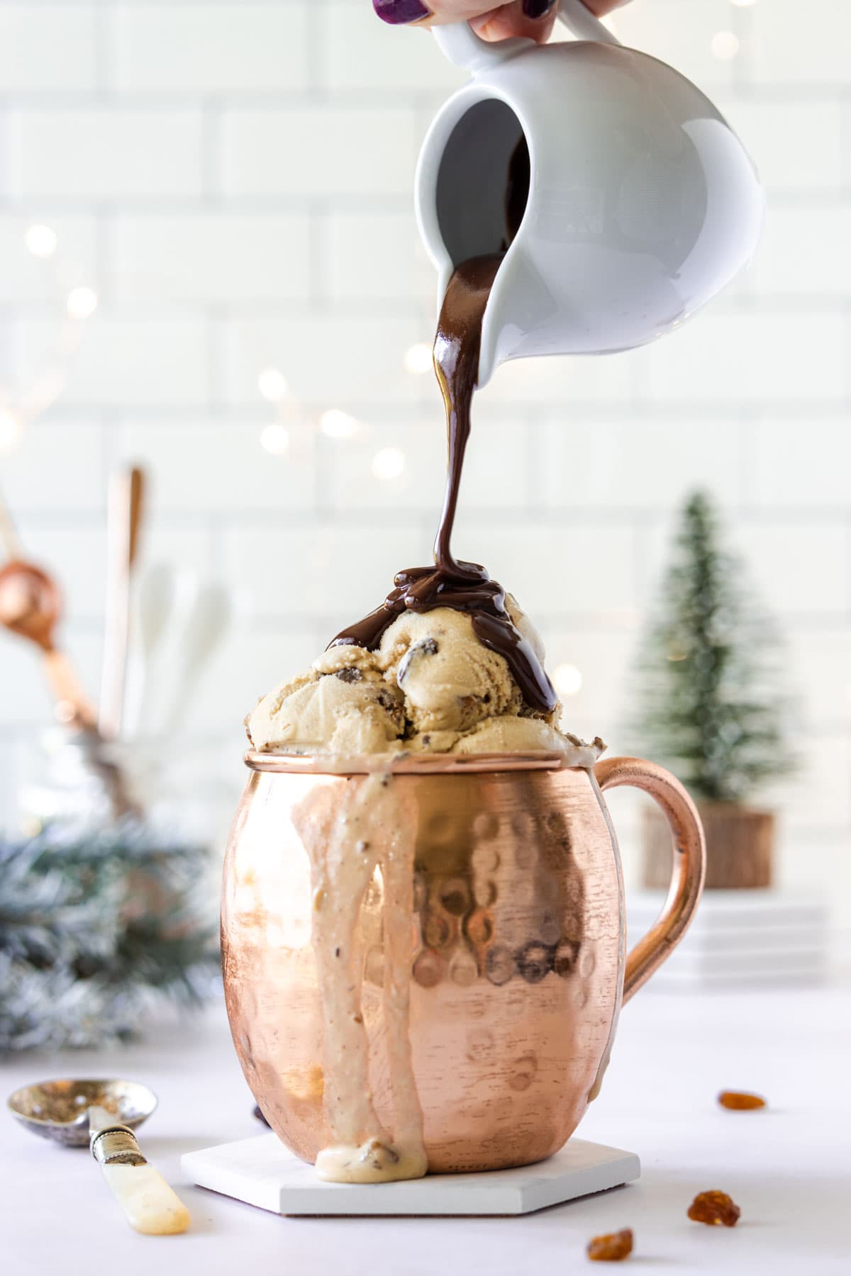 White jug pouring chocolate sauce over the top of ice cream in a copper mug