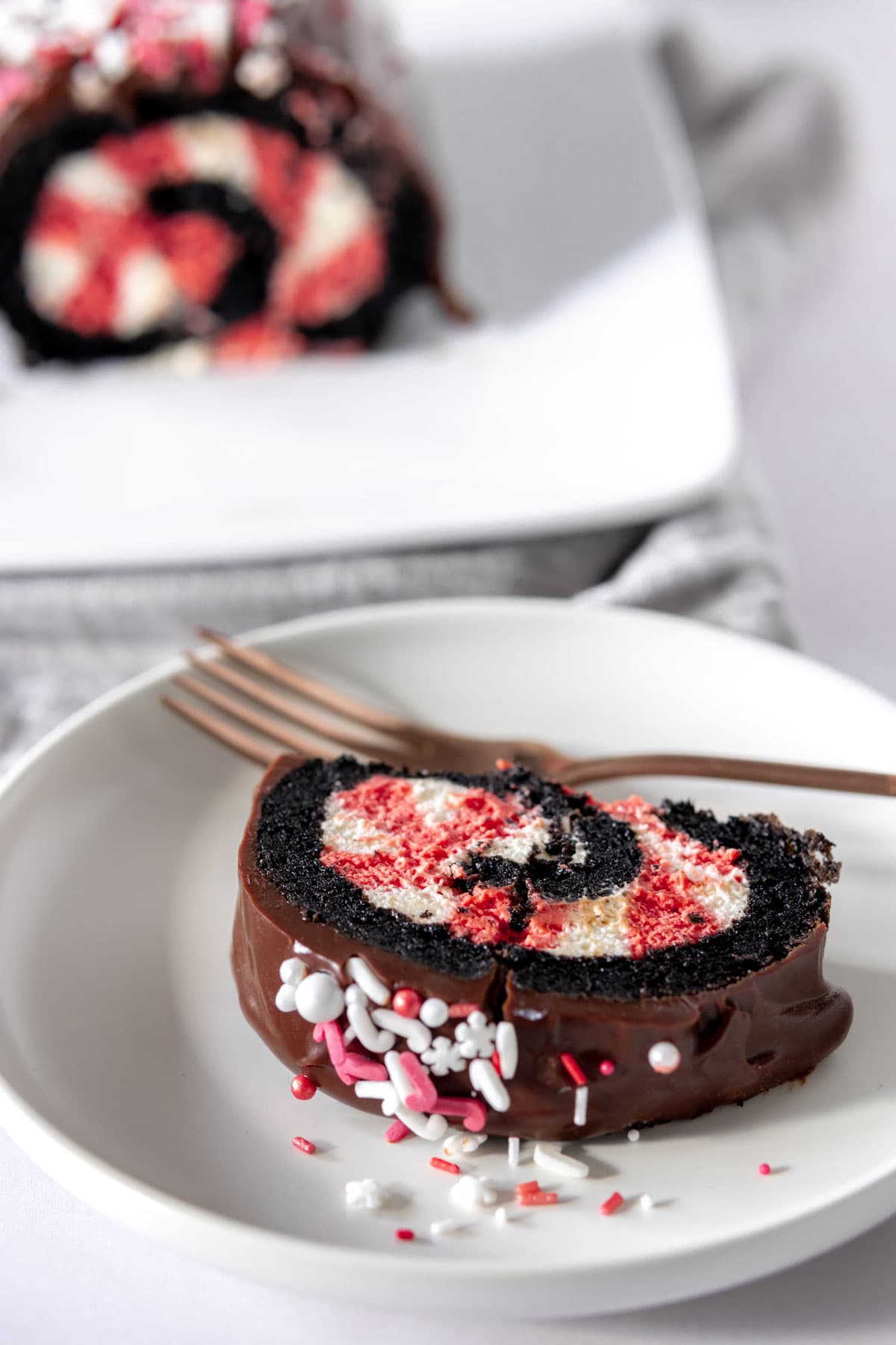 Chocolate roll cake slice filled with red and white cream and sprinkled with red and white sugar sprinkles