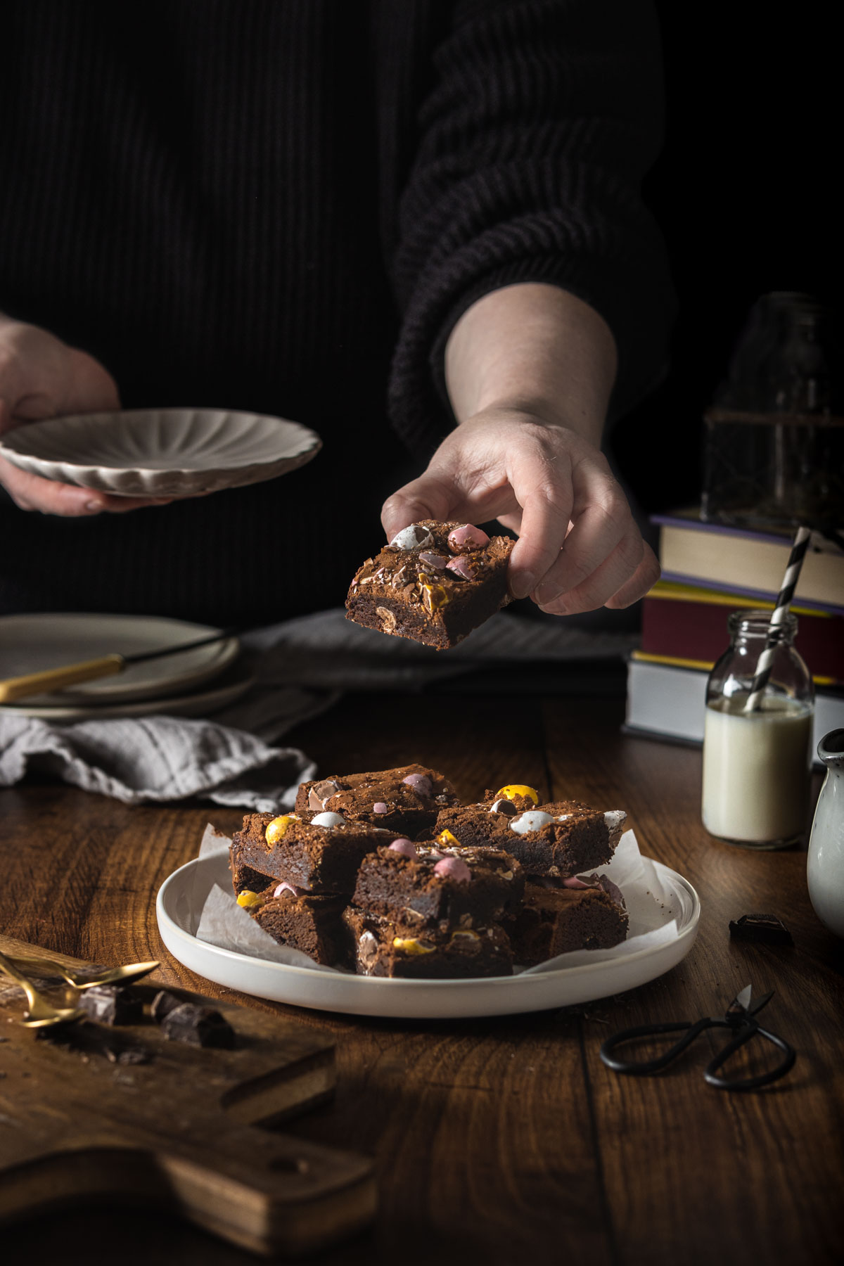 A person picking up a slice of Mini Egg brownies from a serving plate with lots of brownie slices