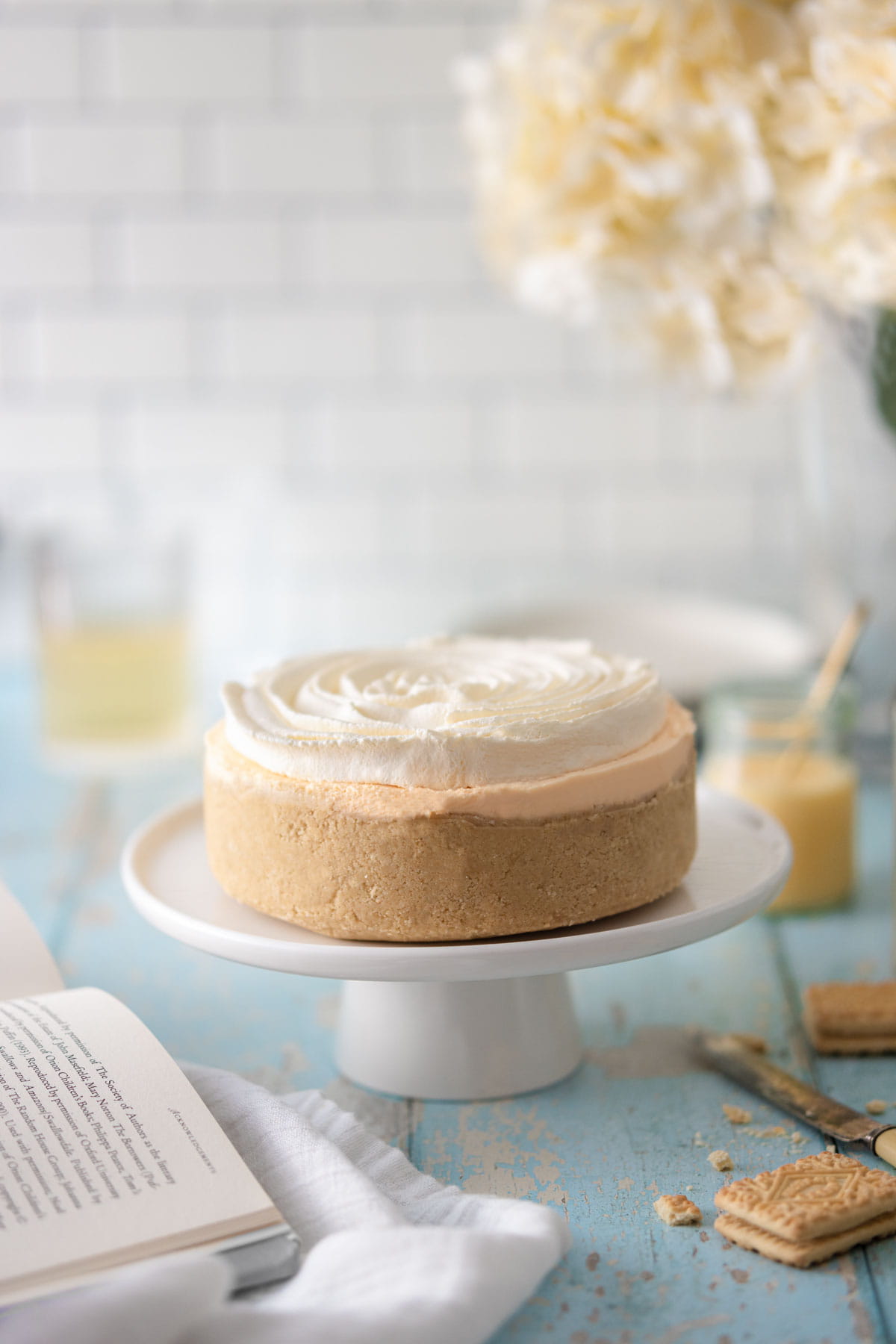A no bake custard cream cheesecake with a swirl of cream on top, on a white cake stand