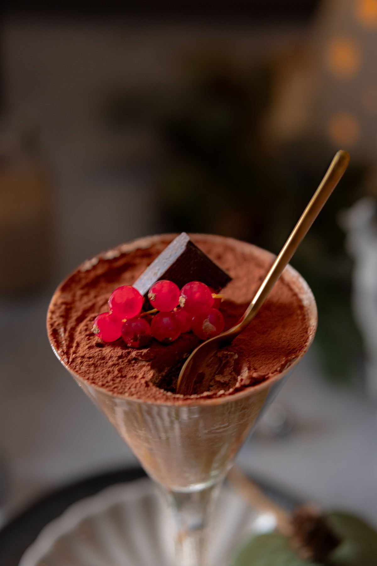 Chocolate mousse in a glass dusted with cocoa powder and topped with red currants and a block of chocolate