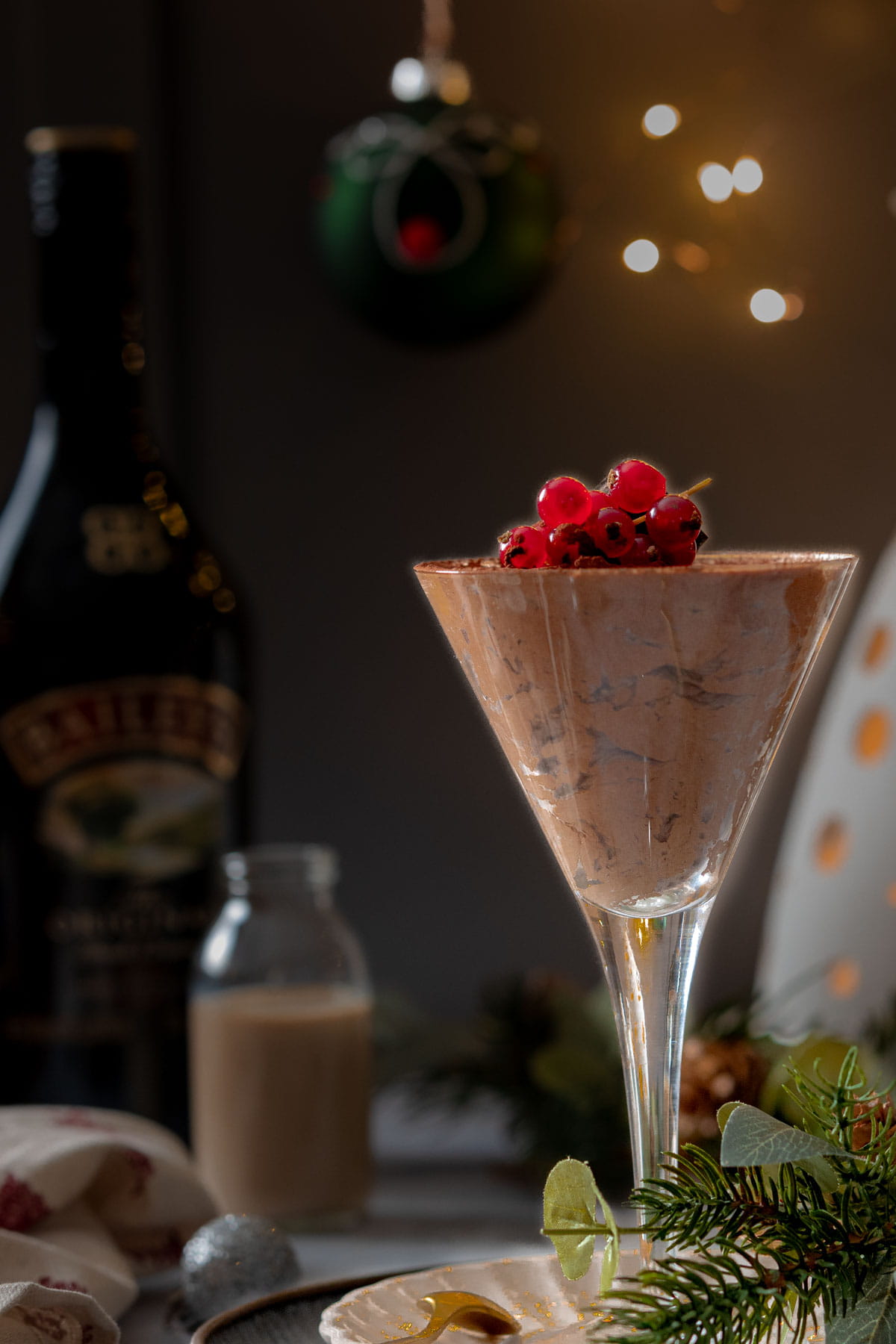 Baileys Chocolate Mousse in a martini glass on a table surrounded by Christmas baubles and fairy lights.