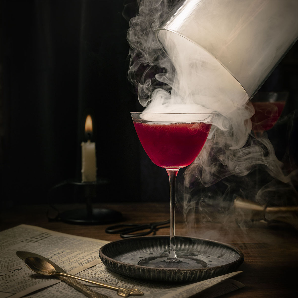 A dark magenta gin and rum cocktail in a coupe glass as cherry smoke curls dramatically around it while the cloche is lifted, captured by Lou Carruthers in moody, candlelit tones.